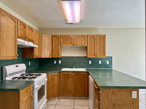 Kitchen featuring gas range gas stove, under cabinet range hood, a peninsula, dark countertops, and tasteful backsplash