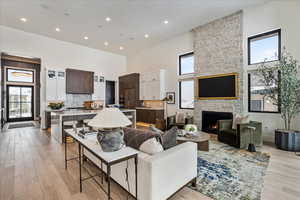 Living room featuring a high ceiling, light wood-style flooring, a fireplace, and recessed lighting