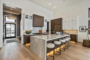 Kitchen with a towering ceiling, light wood-style floors, a breakfast bar, a large island, and light stone countertops