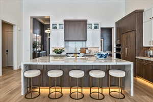 Kitchen with light wood finished floors, glass insert cabinets, and dark brown cabinetry
