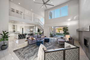Living room with a towering ceiling, a glass covered fireplace, recessed lighting, a ceiling fan, and stairway