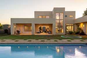 Back of property at dusk featuring an outdoor pool, stucco siding, and a patio