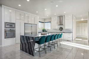 Kitchen featuring built in appliances, wall chimney range hood, a kitchen bar, modern cabinets, and recessed lighting
