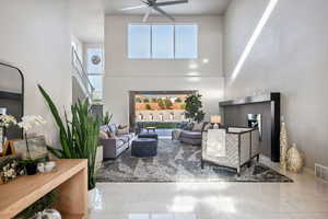 Living area featuring a high ceiling, a ceiling fan, plenty of natural light, stairs, and marble finish flooring