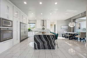 Kitchen featuring built in appliances, wall chimney range hood, decorative backsplash, a center island, and recessed lighting