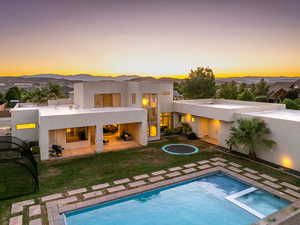 Back of property at dusk featuring stucco siding, a patio area, a pool with connected hot tub, and a yard