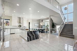 Kitchen featuring white dishwasher, wall chimney range hood, decorative backsplash, recessed lighting, and a center island with sink