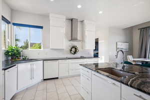 Kitchen featuring white dishwasher, wall chimney exhaust hood, healthy amount of natural light, decorative backsplash, and recessed lighting