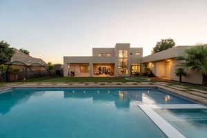 Back of house at dusk with stucco siding, a pool with connected hot tub, and a patio