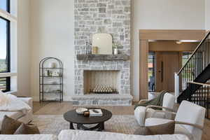 Living room with wood finished floors, stairway, a stone fireplace, and a high ceiling