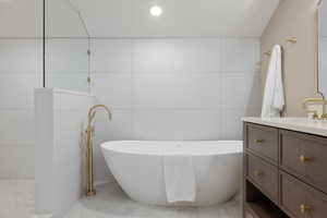 Bathroom featuring vanity, a freestanding bath, a walk in shower, recessed lighting, and tile walls