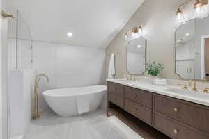 Bathroom featuring double vanity, a freestanding tub, recessed lighting, lofted ceiling, and tile walls