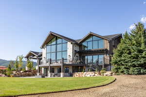 Back of property with a yard, stone siding, a patio area, and a balcony