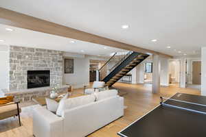 Living area with stairs, light wood-style flooring, recessed lighting, a stone fireplace, and beam ceiling