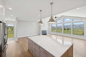 Kitchen featuring open floor plan, stainless steel fridge, light wood-style floors, light stone countertops, and vaulted ceiling