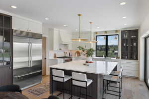 Kitchen featuring premium appliances, light wood finished floors, a kitchen bar, recessed lighting, and white cabinets