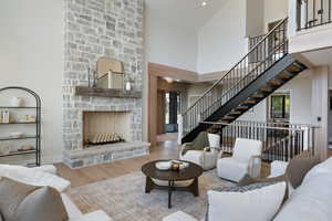 Living room featuring wood finished floors, high vaulted ceiling, plenty of natural light, a stone fireplace, and stairway