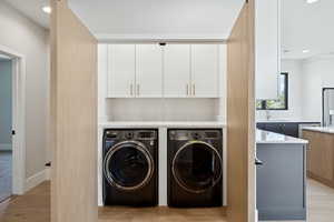 Laundry area with recessed lighting, independent washer and dryer, light wood finished floors, and cabinet space