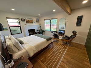 Bedroom with wood finished floors, recessed lighting, beamed ceiling, and a fireplace