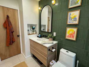 Half bathroom featuring tile patterned flooring, vanity, and tile walls