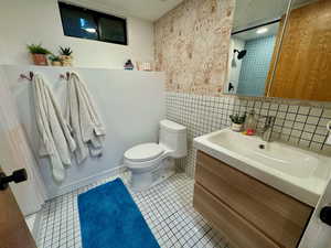 Bathroom with vanity, tile patterned floors, a shower, wallpapered walls, and tile walls