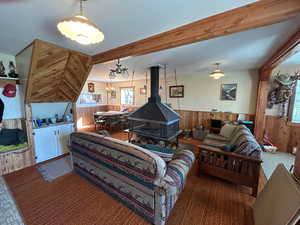 Carpeted living room with a wainscoted wall, wood walls, a chandelier, healthy amount of natural light, and a wood stove