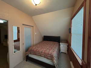 Carpeted bedroom featuring vaulted ceiling and a textured ceiling