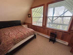 Bedroom with light carpet, vaulted ceiling, a baseboard radiator, wainscoting, and wood walls