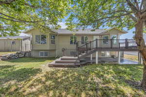 Rear view of property with a wooden deck, a patio, a lawn, a shed, and a shingled roof