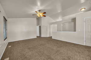 Carpeted empty room featuring a ceiling fan and vaulted ceiling
