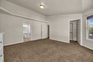 Unfurnished bedroom featuring carpet, a spacious closet, ensuite bathroom, and a closet