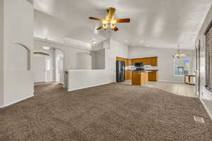 Unfurnished living room with light colored carpet, a chandelier, high vaulted ceiling, a ceiling fan, and recessed lighting