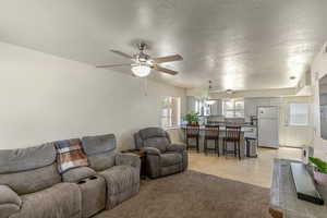 Living area featuring a textured ceiling, ceiling fan, light tile patterned floors, and light colored carpet