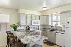 Kitchen with white appliances, a peninsula, a breakfast bar, light stone counters, and light tile patterned floors