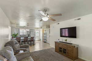 Living room with a ceiling fan, light tile patterned floors, and light colored carpet