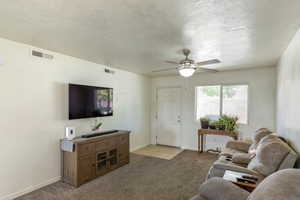 Living room with light colored carpet, a ceiling fan, and a textured ceiling