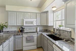 Kitchen featuring white appliances, light tile patterned floors, and stone counters