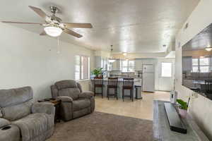 Living area with a textured ceiling, healthy amount of natural light, a ceiling fan, and light tile patterned floors