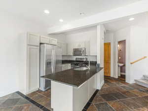 Kitchen with stainless steel appliances, stone tile flooring, a peninsula, recessed lighting, and dark stone countertops
