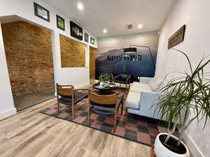 Living area with wood finished floors, recessed lighting, and brick wall