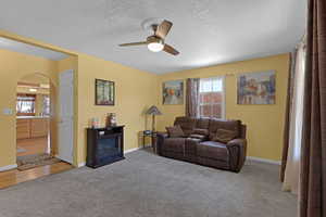 Living area featuring arched walkways, a ceiling fan, carpet flooring, and a textured ceiling