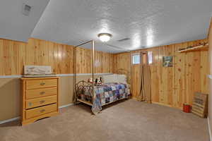 Bedroom with wooden walls, carpet, and a textured ceiling