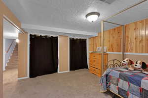 Carpeted bedroom featuring a textured ceiling and wood walls