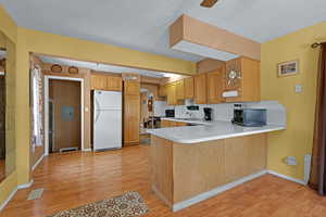 Kitchen featuring freestanding refrigerator, light wood-style floors, a peninsula, light countertops, and a textured ceiling