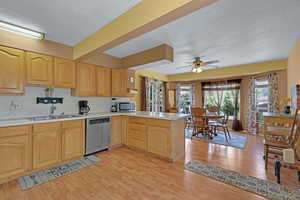 Kitchen with stainless steel appliances, light wood-style floors, a textured ceiling, light countertops, and a peninsula