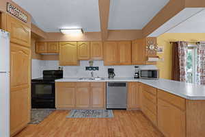 Kitchen with stainless steel appliances, a peninsula, light countertops, light wood finished floors, and beam ceiling