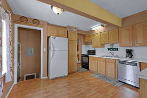 Kitchen with freestanding refrigerator, dishwasher, black electric range oven, light countertops, and light wood-type flooring