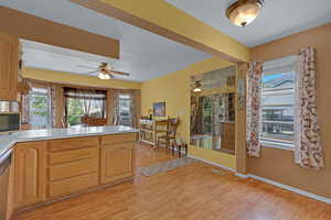 Kitchen with ceiling fan, light wood-style floors, black microwave, light countertops, and a peninsula