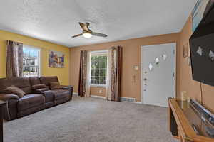 Living area with ceiling fan, a textured ceiling, and carpet flooring