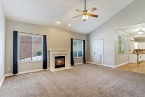Unfurnished living room featuring light carpet, healthy amount of natural light, a ceiling fan, lofted ceiling, and a tiled fireplace